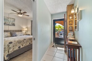 A bedroom with a bed, a ceiling fan, and a nightstand. There is a door leading to a balcony with a view of the outside.