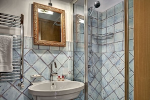 A bathroom with a white sink, a mirror with an ornate frame, and a shower with blue mosaic tiles. - Stony Villa Volcano View (Massa Lubrense)