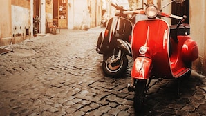Une ruelle étroite pavée de pierres, où sont garés des scooters anciens le long du trottoir.