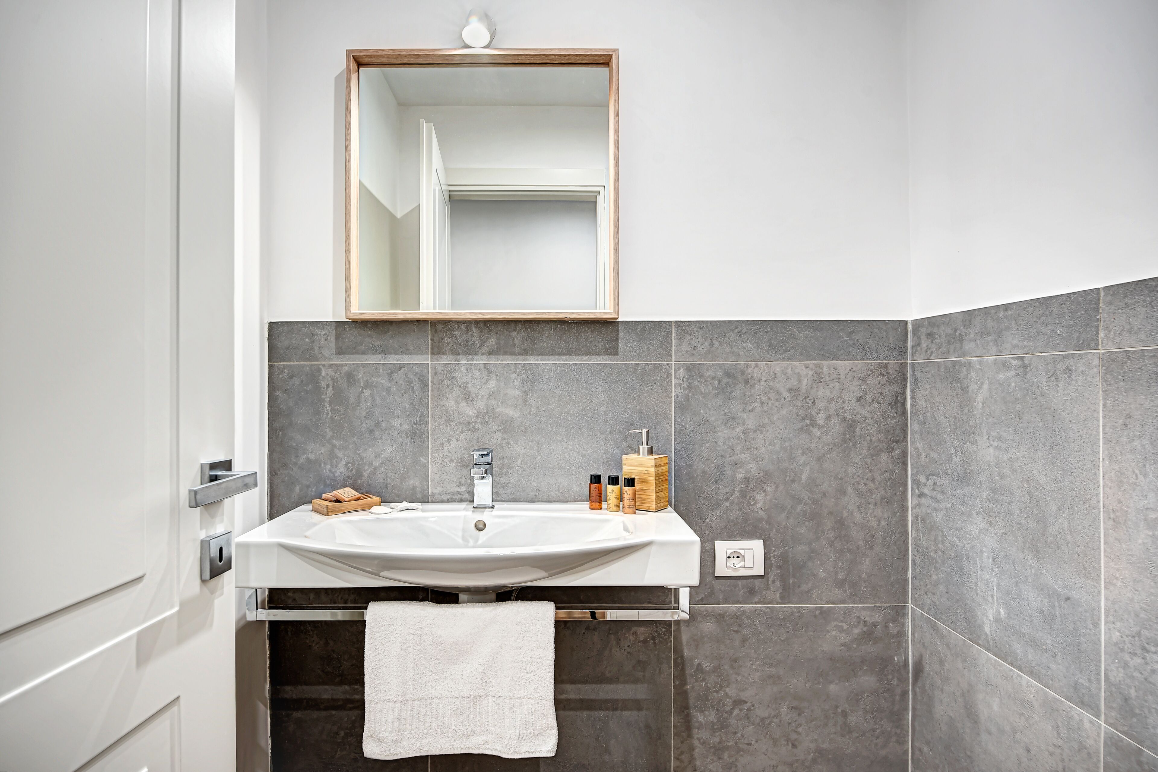 A modern bathroom with a white sink, a wooden medicine cabinet, and a large mirror.