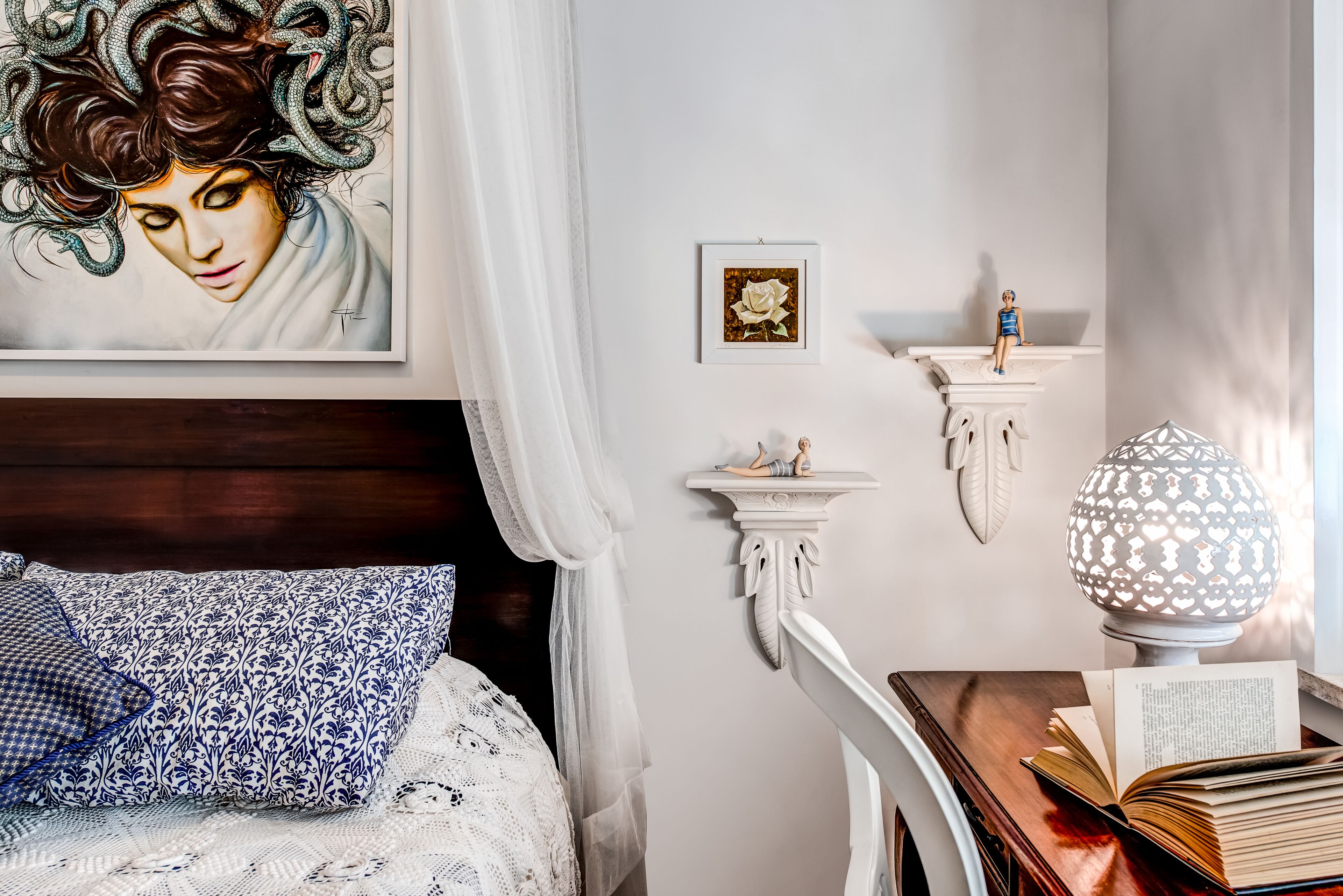 Un dormitorio con una cama, una mesita de noche con lámpara, un cuadro enmarcado y una pequeña figurita.