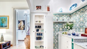 Une cuisine avec des meubles blancs, un meuble blanc doté de portes en verre et un pare-feu en carreaux avec un motif bleu et vert.