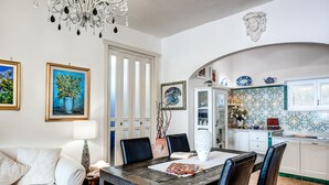 Un coin repas avec une table en bois, des chaises noires, un canapé blanc et un lustre.