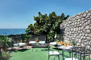 Um pátio externo com parede de pedra, assentos e uma mesa posta para refeições.