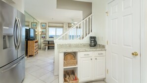 A kitchen with white cabinets, a stainless steel refrigerator, a coffee maker, and a view of the ocean through the windows.