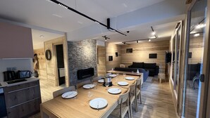 A modern kitchen with a long wooden table set for dining, a stone wall, and a built-in TV. - BOREAL - Lovely apartment in the village center and close to the slopes - Wi-Fi - Garage (La Clusaz)