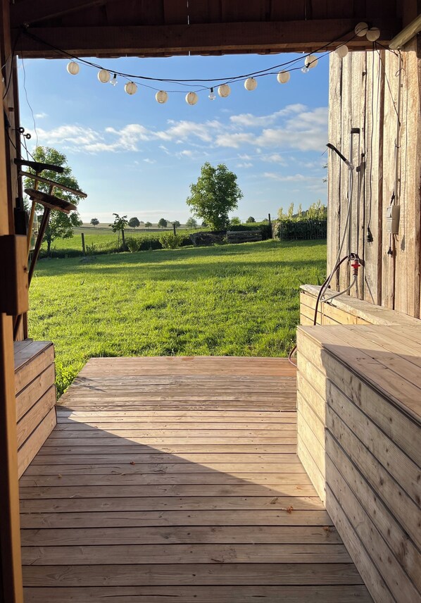 Een houten terras met uitzicht op een groen veld en een houten gebouw.