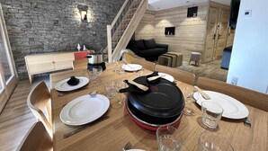 A dining area with a wooden table set for four, a stone wall, and a staircase leading to another level. - POLARIS - Lovely apartment in the village center and close to the slopes - Wi-Fi - Garage (La Clusaz)