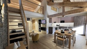 A spacious loft-style apartment with a high ceiling, exposed wooden beams, a dining area, kitchen, and a cozy seating area with a staircase. - POLARIS - Lovely apartment in the village center and close to the slopes - Wi-Fi - Garage (La Clusaz)