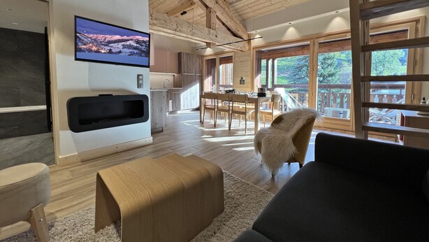 A spacious living area with a wooden ceiling, a mounted TV, a dining area, and large windows offering a view of the outdoors. - POLARIS - Lovely apartment in the village center and close to the slopes - Wi-Fi - Garage (La Clusaz)