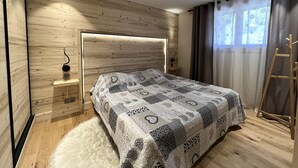 A modern bedroom with a wooden headboard, a patterned bedspread, a fluffy rug, and a wooden ladder against the wall. - POLARIS - Lovely apartment in the village center and close to the slopes - Wi-Fi - Garage (La Clusaz)