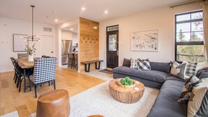 A modern living room with a wooden dining table, black and white checkered chairs, a grey sofa, and a round wooden coffee table. - Tremblant Prestige - Les Eaux 215-6 (Mont-Tremblant)