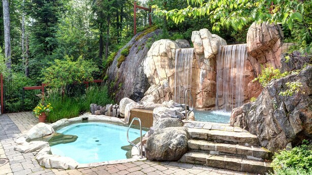 A naturalistic outdoor pool area with a waterfall, surrounded by rocks and greenery. - Tremblant Prestige - Les Eaux 215-6 (Mont-Tremblant)