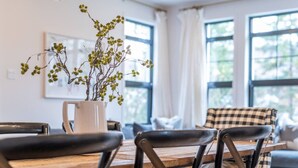 A dining area with a wooden table, black chairs, a white vase with green branches, and a pendant light with clear glass shades. - Tremblant Prestige - Les Eaux 215-6 (Mont-Tremblant)