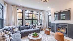 A modern living room with a grey sofa, round wooden coffee table, and a fireplace. - Tremblant Prestige - Les Eaux 215-6 (Mont-Tremblant)