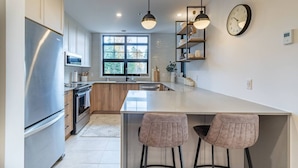 A modern kitchen with a large island, stainless steel appliances, pendant lighting, and a view of the outdoors. - Tremblant Prestige - Les Eaux 215-6 (Mont-Tremblant)