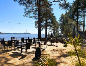 An outdoor seating area with tables and chairs, overlooking a body of water with wind turbines in the distance. - Beach Hotel Santalahti (Kotka)
