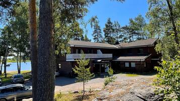 A lodge with a large rock in the foreground, a parking area with cars, and a view of the lake.