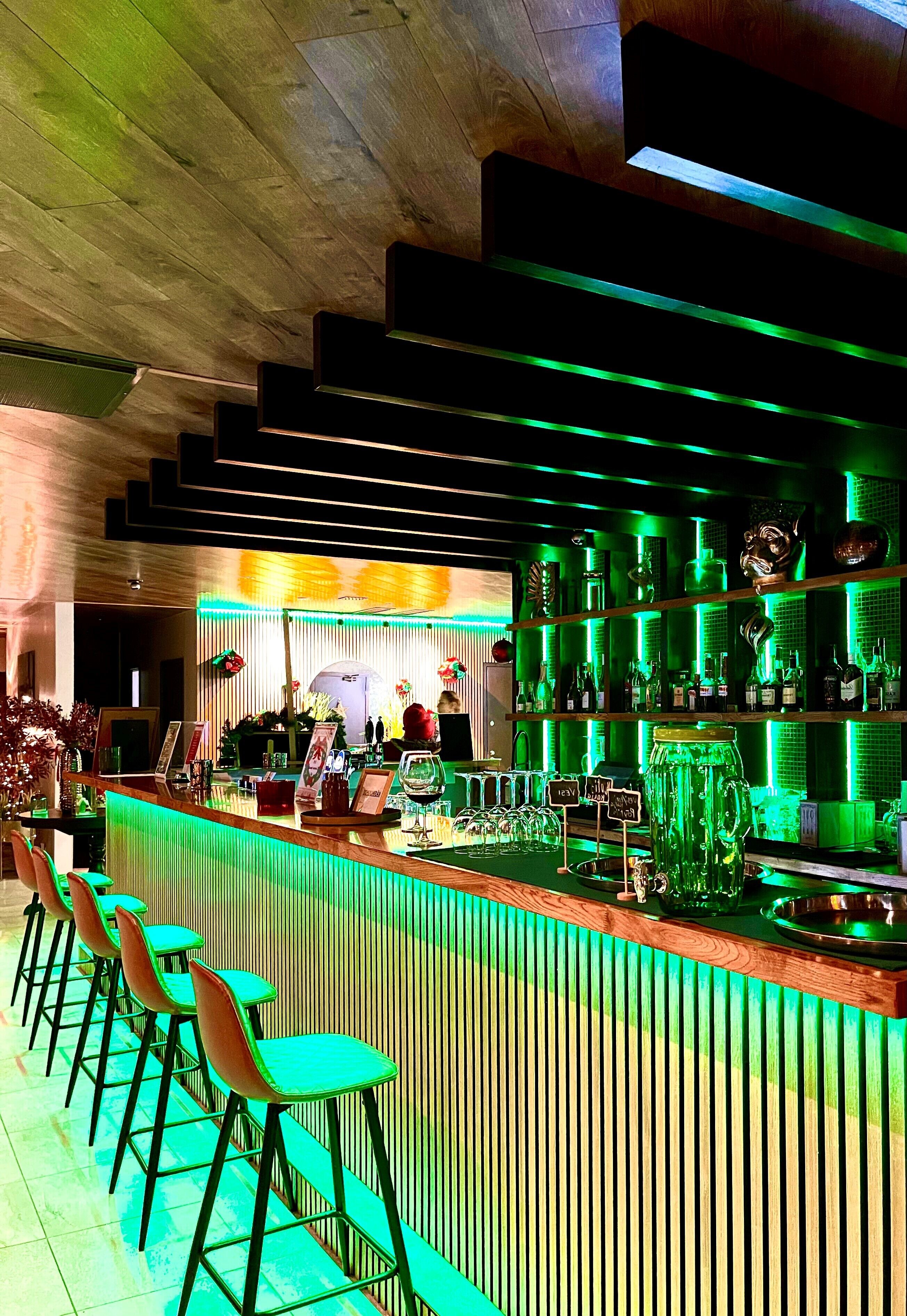 A bar area with a long counter, multiple stools, and shelves stocked with bottles.