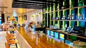 A bar area with wooden bar counter, orange cushioned bar stools, and shelves stocked with bottles.