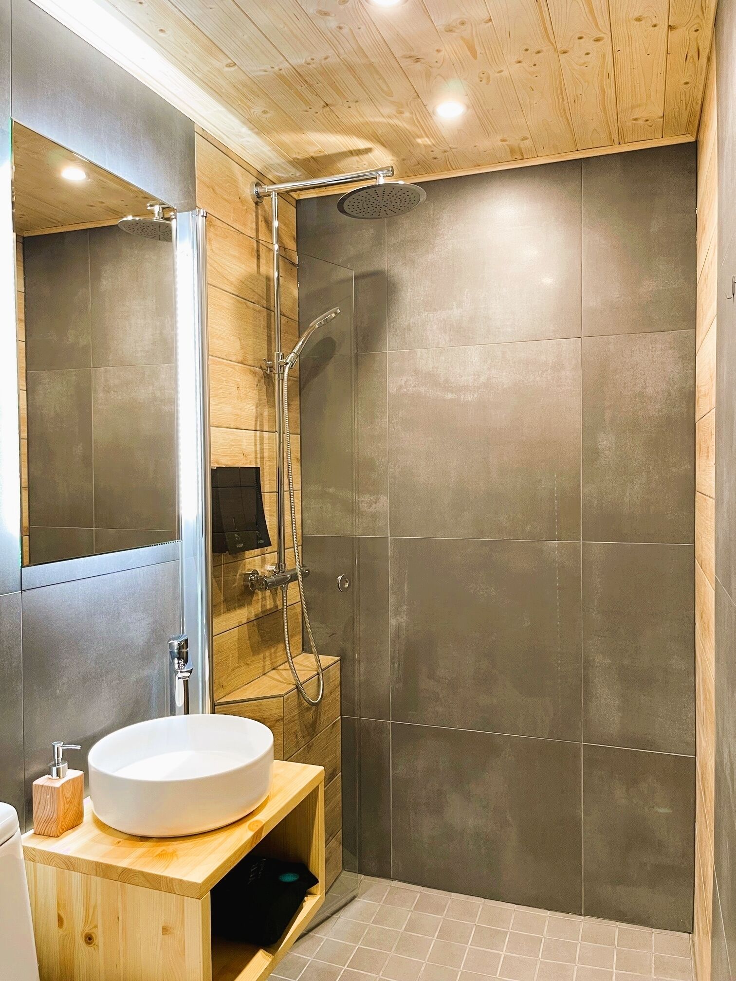 A modern bathroom with a wooden vanity, a large mirror, a round sink, and a walk-in shower with a glass door.