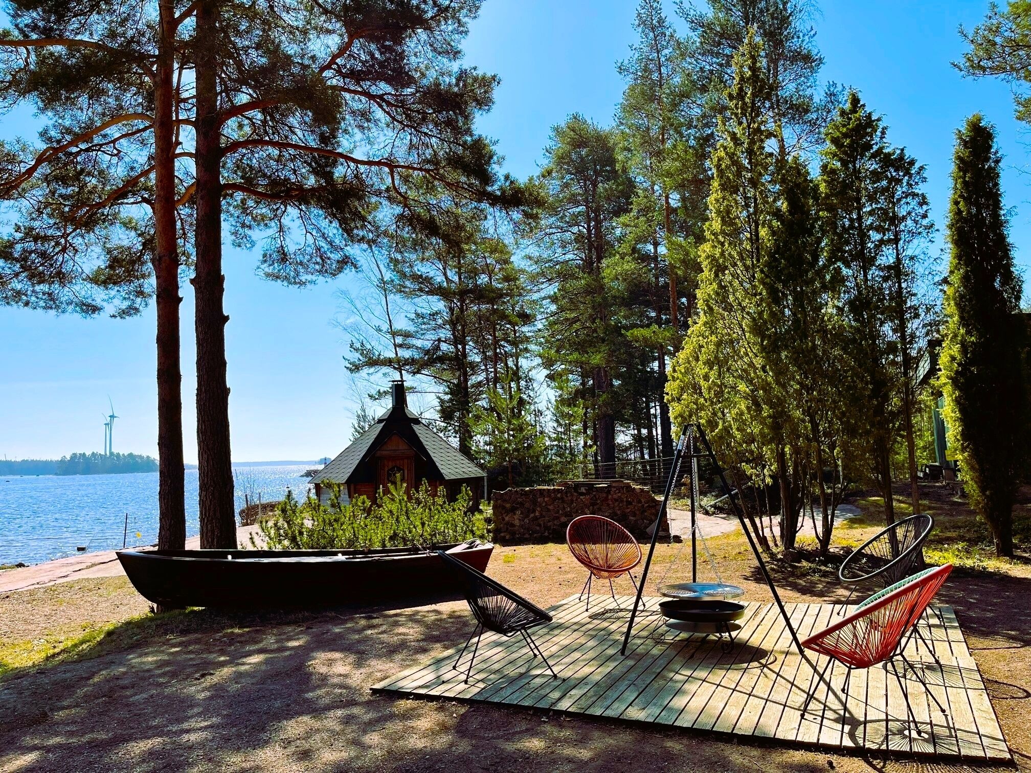 A lakeside cabin with a deck, outdoor seating, and a boat.