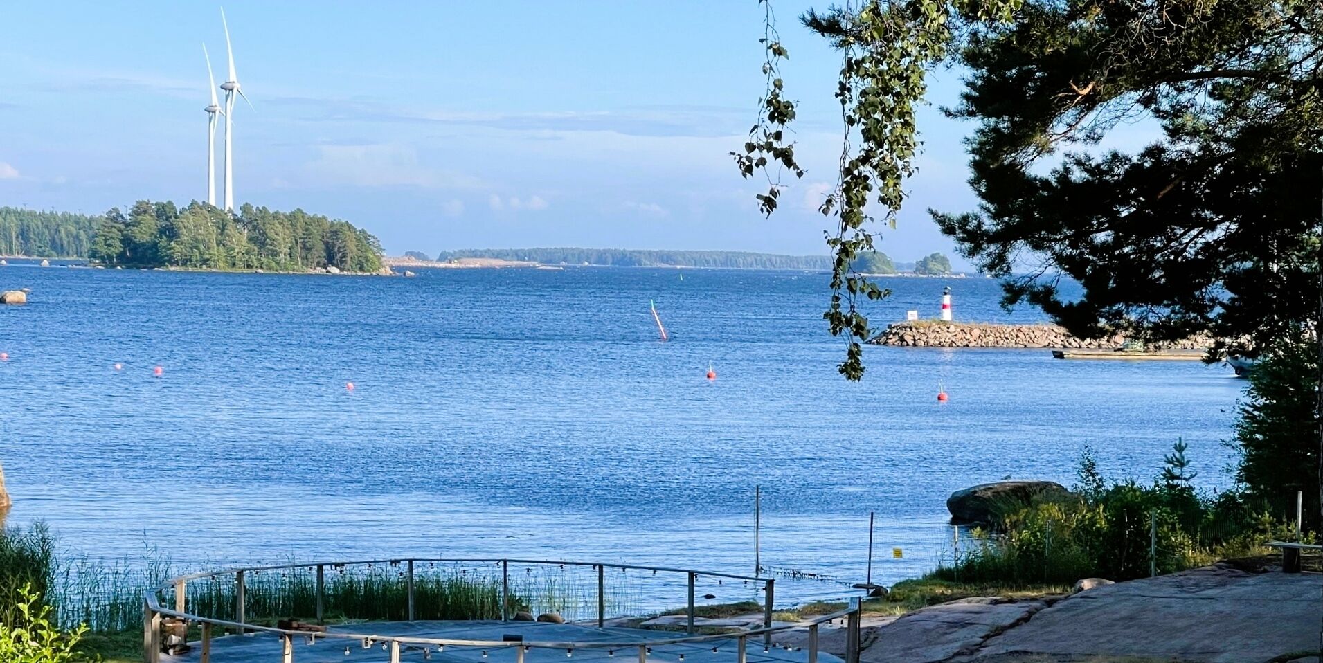 Näkymä merenrannalta, jossa näkyy majakka, tuulivoimaloita ja kivikkoinen rantaviiva.