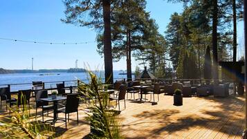 An outdoor deck with wooden flooring, surrounded by tall trees and overlooking a body of water.