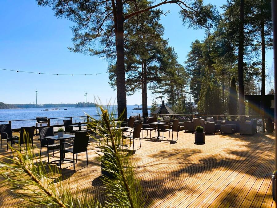 An outdoor deck with wooden flooring, surrounded by tall trees and overlooking a body of water.