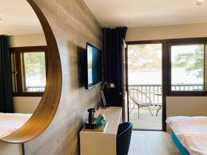 A hotel room with a curved wooden wall, a desk with a kettle and a bottle, a TV, two beds, and a balcony with a chair. - Beach Hotel Santalahti (Kotka)