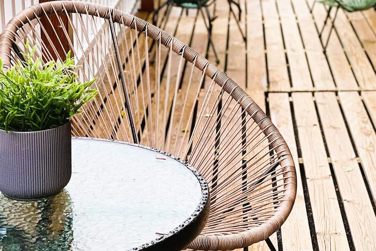 A wooden deck with wicker chairs and a table, surrounded by a white fence.