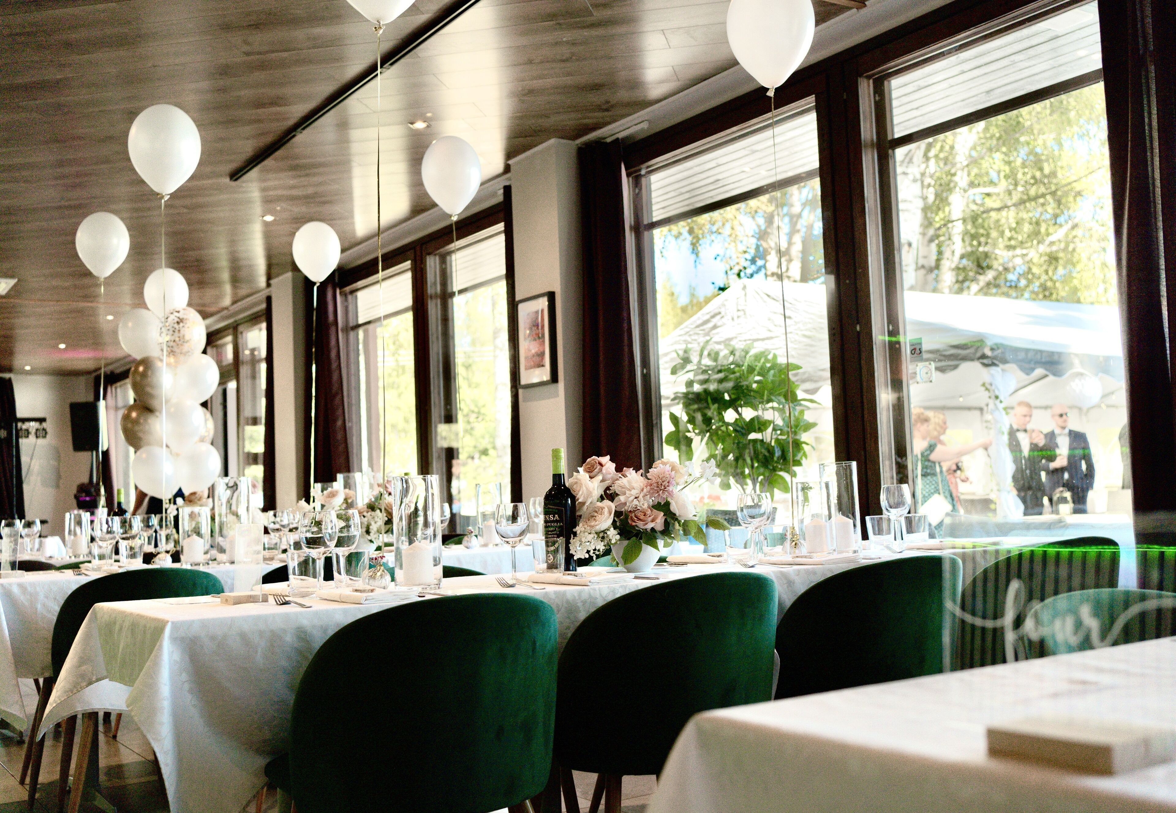 Un restaurante con mesas dispuestas para comer, ventanas amplias y globos decorativos.