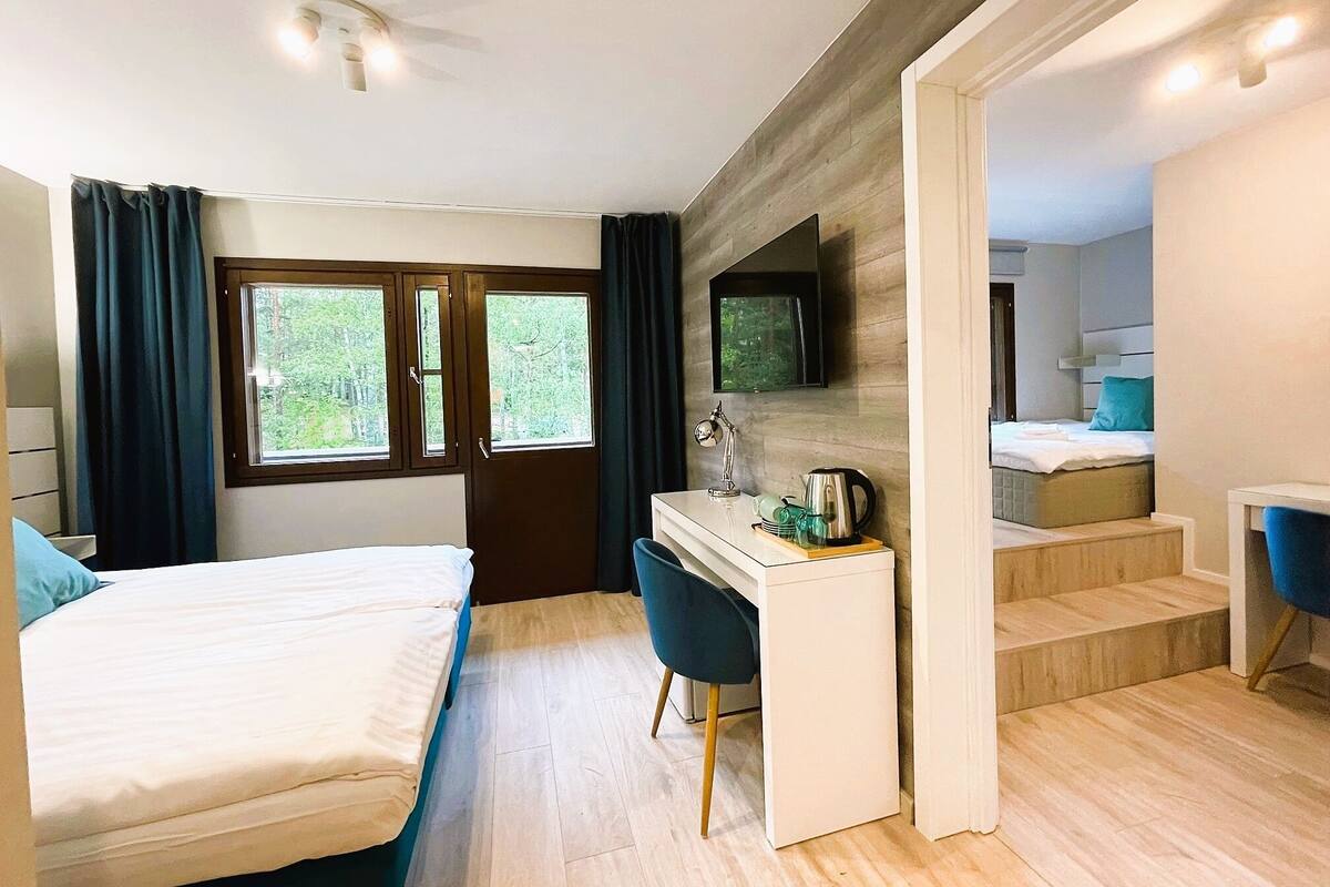 A modern bedroom with a bed, desk, and a view of greenery outside.