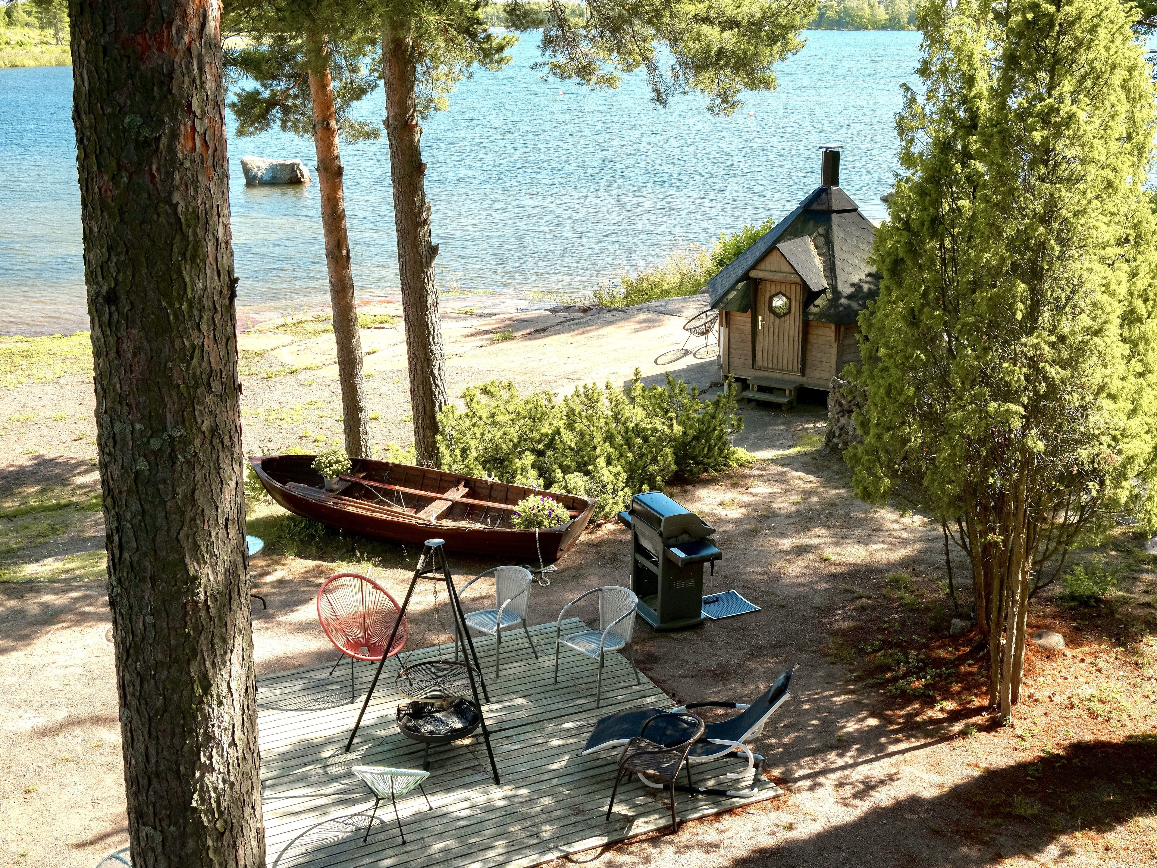 A lakeside cabin with a boat, outdoor seating, and a small shed.