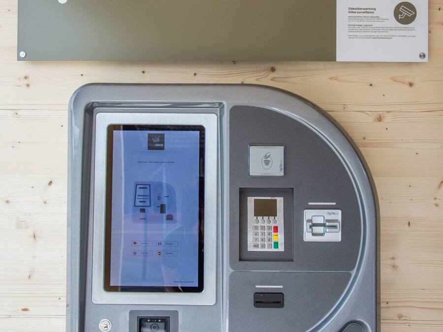 A check-in kiosk with a screen, keypad, and card reader, mounted on a wooden wall.