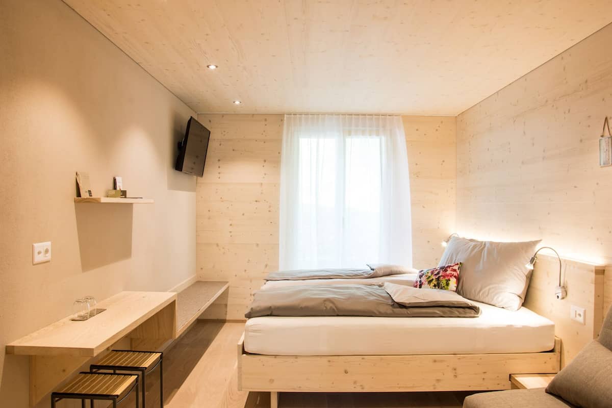Un dormitorio con cama, mesita de noche y televisor montado en la pared.