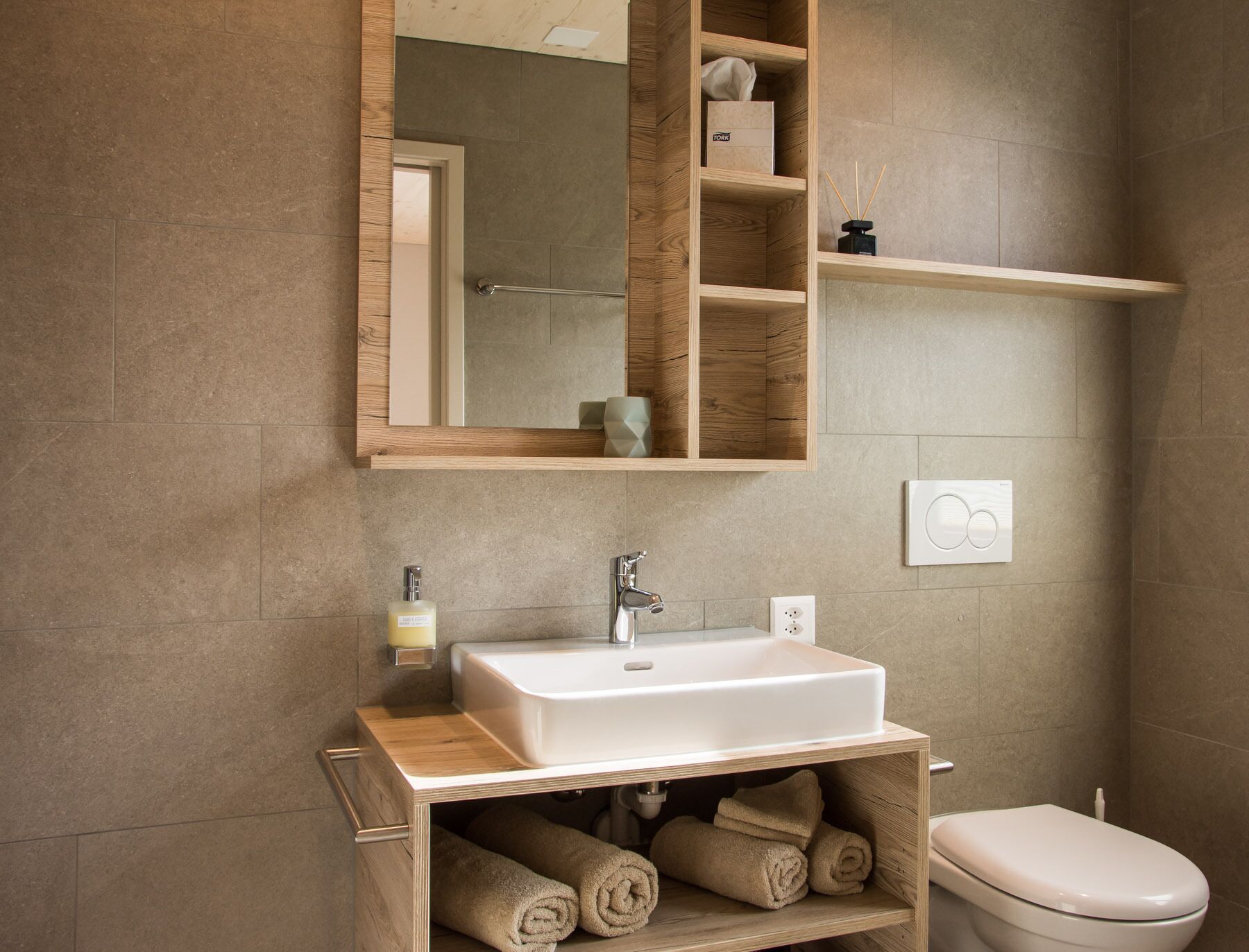 A bathroom with a wooden vanity, a white sink, a mirror, and a toilet.