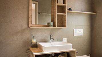 Un baño con un tocador de madera, un lavabo blanco, un espejo y un inodoro.