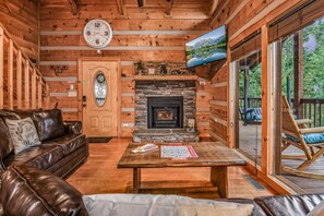 L’intérieur chaleureux d’un chalet avec une cheminée en pierre, un canapé en cuir et un téléviseur fixé au mur.