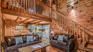 A wooden cabin interior with a staircase, two leather sofas, a dining table, and a kitchen area. - A-bluff & Beyond 2 Bedroom Cabin by RedAwning (Sevierville)