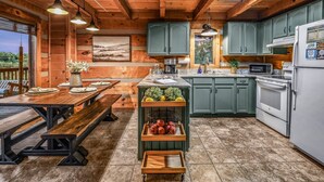 A rustic cabin kitchen with wooden beams, a dining table with benches, a fruit basket, and a refrigerator. - A-bluff & Beyond 2 Bedroom Cabin by RedAwning (Sevierville)