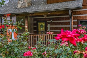 Une cabane en bois avec un porche, un mur en pierre et un jardin où poussent des rosiers.