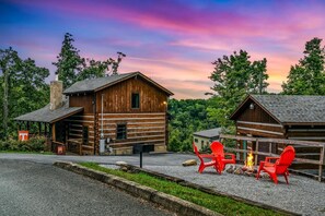 A rustic cabin with a stone chimney, a covered porch, and a fire pit with red chairs. - A-bluff & Beyond 2 Bedroom Cabin by RedAwning (Sevierville)
