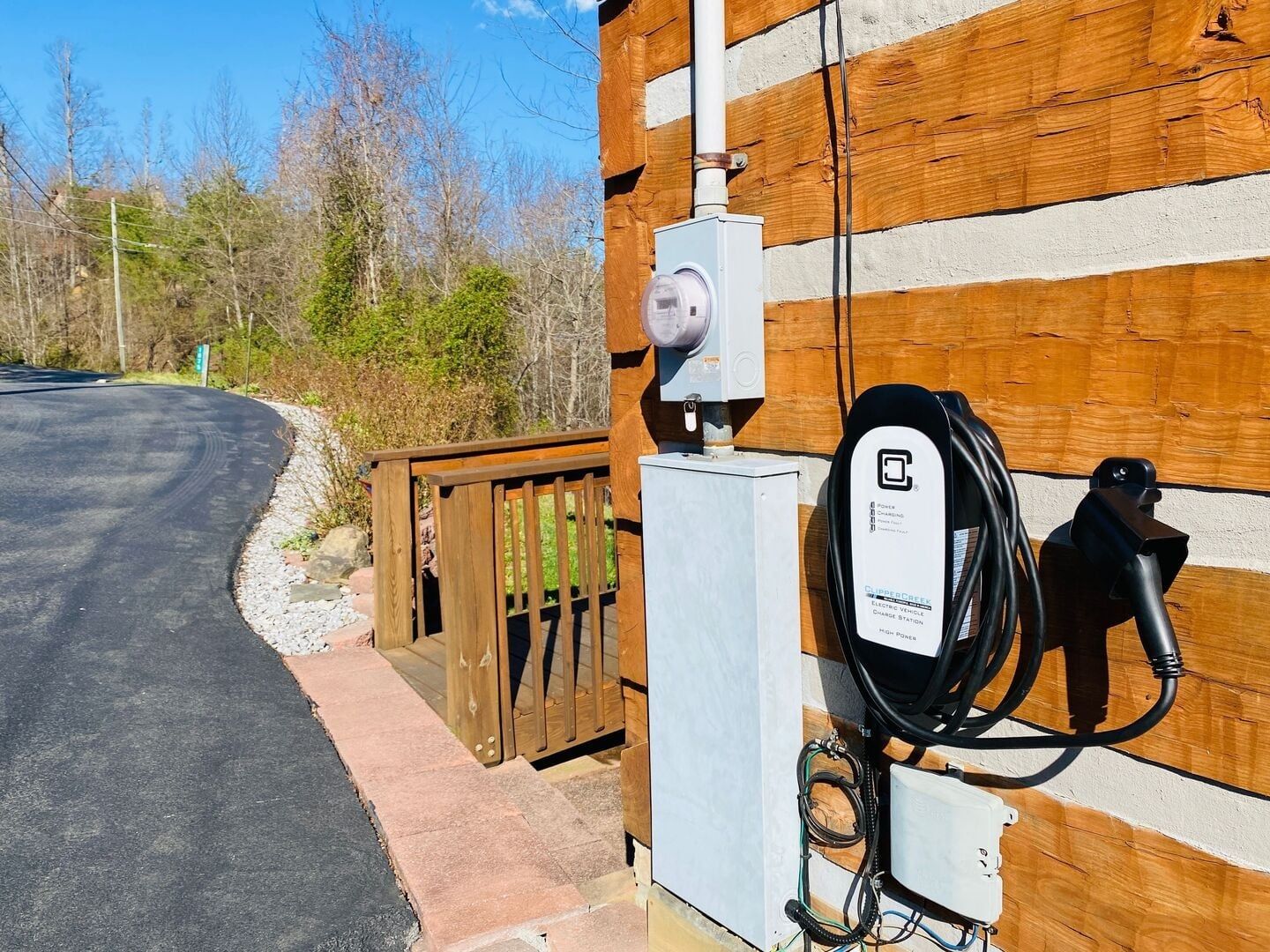 En laddstation för elfordon med en kabel som är ansluten till ett fordon, monterad på en byggnad med träpanel.