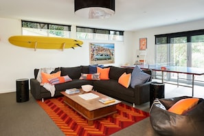 A modern living room with a sofa, coffee table, and a surfboard on the wall. - Seaview House Luxury Coastal Escape Lorne (Lorne)