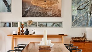 A dining area with a wooden table, black chairs, a woven pendant light, and a wall-mounted shelf with decorative items. - Seaview House Luxury Coastal Escape Lorne (Lorne)