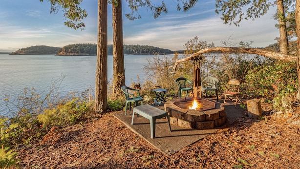 Un espace extérieur aménagé au bord du lac, avec un foyer, des bancs et des chaises.