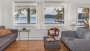 Un salon avec vue sur un lac, une table en bois et un canapé gris.