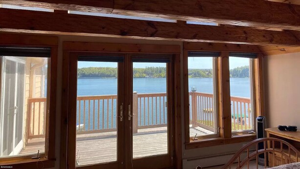 A room with large sliding glass doors leading to a deck overlooking a lake. - Lake Front Home in Heart of the Berkshires Near Jiminy Peak (Pittsfield)