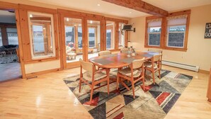 A dining area with a wooden table and chairs, large windows, and a view of the outdoors. - Lake Front Home in Heart of the Berkshires Near Jiminy Peak (Pittsfield)